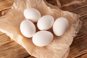 Rustic chicken eggs on parchment paper on a wooden plank table. The view from the top.