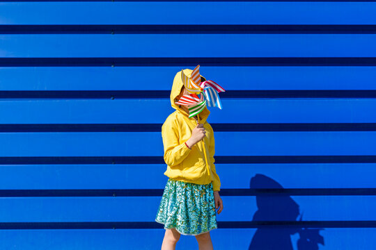 Little girl standing in front of blue background hiding behind pinwheel