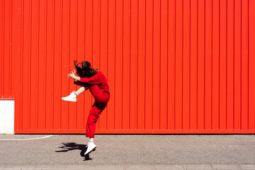 Woman dressed in red overall jumping in the air in front of red roller shutter