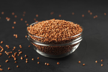 Buckwheat in a glass plate and scattered on the black table.