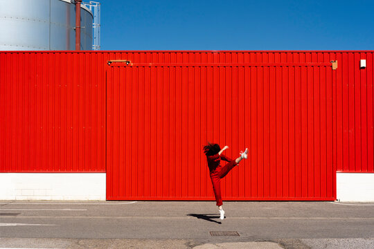 Woman dressed in red overall jumping in the air in front of red roller shutter