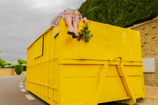Woman lying on top of yellow container, holding buch of flowers