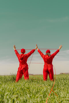 Back view of young couple wearing red overalls and hats performing on a field with red string