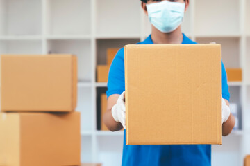 Delivery man holding cardboard boxes in medical rubber gloves and mask.