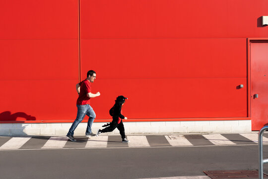 Man running together with his little girl wearing black fancy dress on zebra crossing