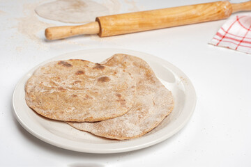 Flatbread on a white plate against the background of rolling pin and rolled dough