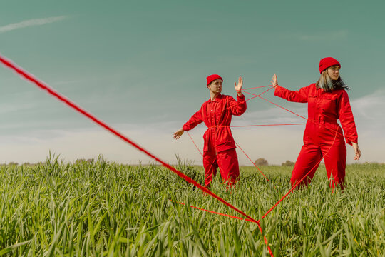 Young couple wearing red overalls and hats performing on a field with red string