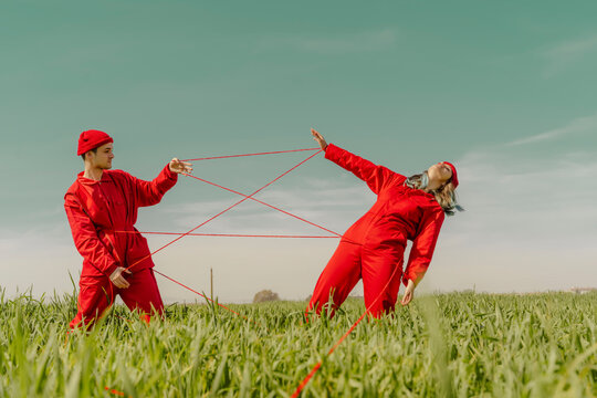 Young couple wearing red overalls and hats performing on a field with red string