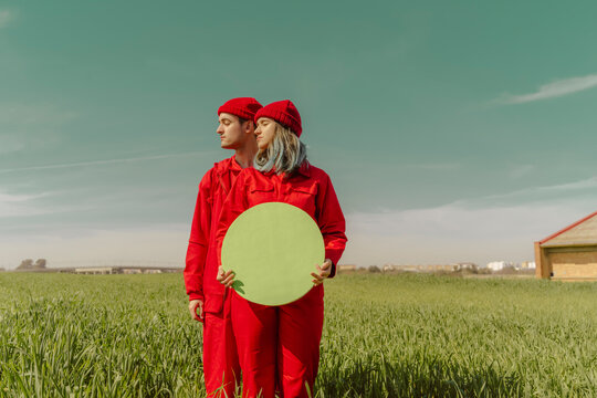 Young couple wearing red overalls and hats standing on a field with green circle