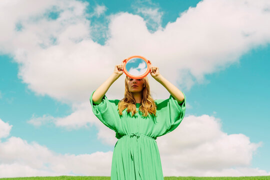 Young woman wearing green dress holding reflecting mirror