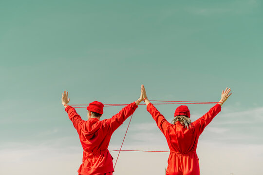 Back view of young couple wearing red overalls and hats performing with red string outdoors