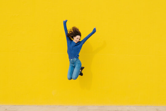 Young woman jumping in the air in front of yellow background