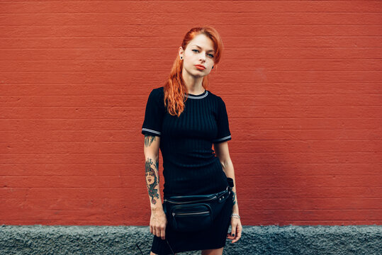 Portrait of red-haired tattooed woman standing at a brick wall