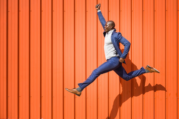Businessman jumping in the air in front of orange wall