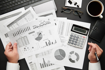 Top view of businessman's hands working with financial reports. Modern black office desk with laptop, notebook, pencil and a lot of things. Flat lay table layout.