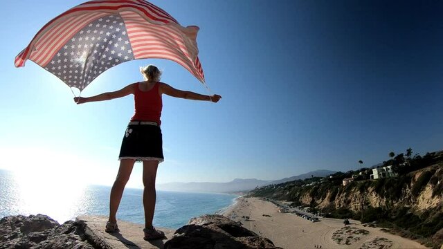 SLOW MOTION: American flag against the sky at Point Dume State Beach from Point Dume promontory on Malibu coast, Pacific Ocean in CA, United States. California West Coast.