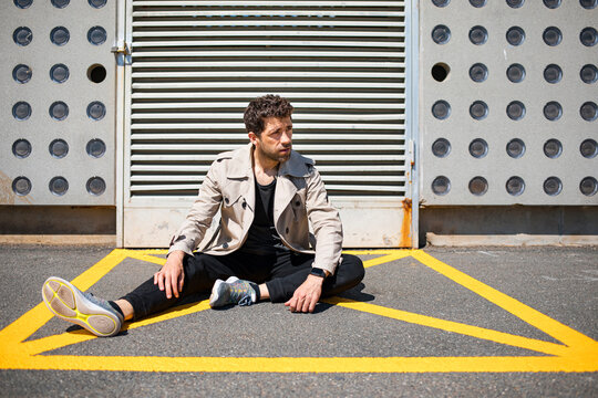 Helpless man sitting on ground in yellow marked area in front of concrete wall