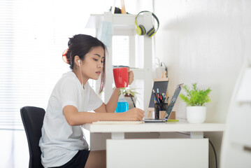 Obraz na płótnie Canvas Asian women work at home according to government policies to prevent communicable diseases. She works hard and her hands hold a red coffee cup. She drinks when she is sleepy.