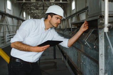 Close up of young Caucasian smiling worker with helmet on head using tablet for work while standing in warehouse.