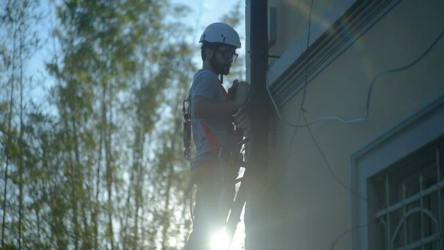 Builder worker using his tools standing on ladder in construction site, with safety equipment and hard hat.