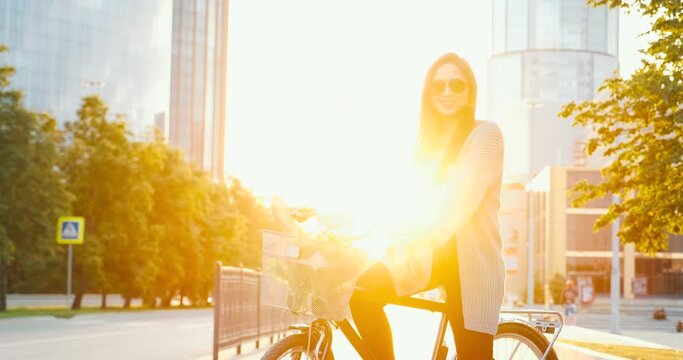 Beautiful girl with classical bike in city at sunset near modern office building
