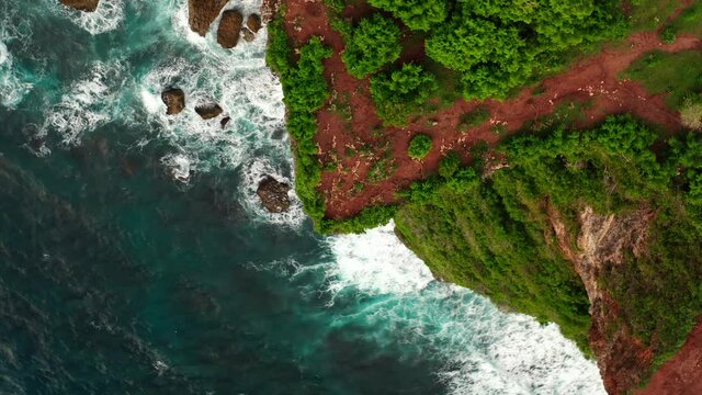 Aerial view from above on a tropical island and ocean waves crashing and foaming against sand beach. Bird's eye aerial shot of golden beach meeting deep blue ocean water. Tourism concept after covid.