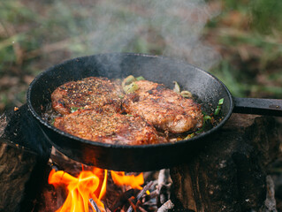 Frying meat in a pan over an open fire with leek. Steak in a pan on a fire. Cooking in nature. Picnic. Grill on fire..