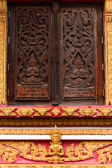 Praying buddha image as wood carving on a window in a temple and religious site in Siamese Lao PDR, Southeast Asia