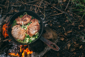 Frying meat in a pan over an open fire with leek. Steak in a pan on a fire. Cooking in nature. Picnic. Grill on fire..