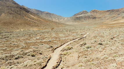 Panorama-Aufnahme einer Wüstenlandschaft mit einer befestigten Piste, die in ein Tal führt, fotografiert mit einer Kameradrohne