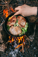 Frying meat in a pan over an open fire with leek. Steak in a pan on a fire. Cooking in nature. Picnic. Grill on fire. Hand with a wooden spatula..