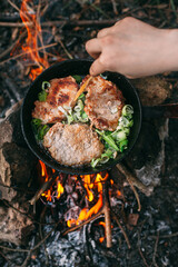 Frying meat in a pan over an open fire with leek. Steak in a pan on a fire. Cooking in nature. Picnic. Grill on fire. Hand with a wooden spatula..