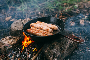 Roasting sausages in a frying pan over an open fire. Preparing food in nature. Lunch in the open...