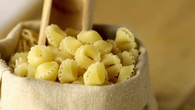 Italian raw uncooked pasta sorprese in linen bag with wooden ladle on wooden table. Motion video close up. Concept of healthy eating