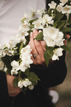A girl in a white shirt holds a bouquet of flowers, an engagement ring on her hand, closeup photo. French manicure on hand
