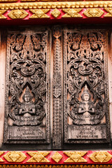Entrance door with wooden carvings of religious buddha images in a temple in Siamese Lao PDR, Southeast Asia