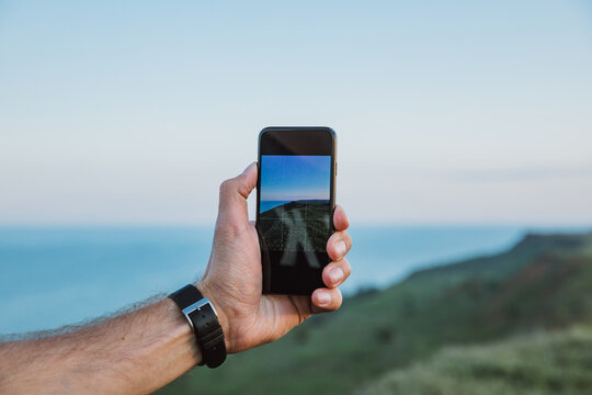 a man holds a phone and takes a picture of the beautiful landscape of the sea, rocks, clouds, sunset, birds