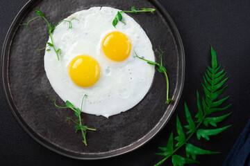 Breakfast with two fried eggs and herbs on black background