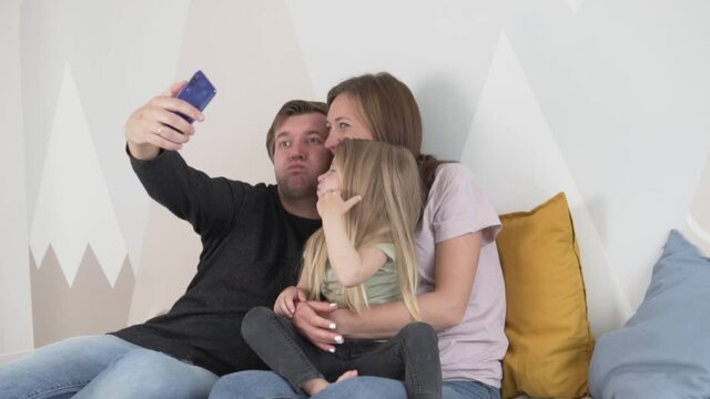 Happy Bonding Family Of Three Sitting On Bed In The Children's Room, Father Taking Selfie Mobile Phone, Watch Ingsituated Photos On Your Phone