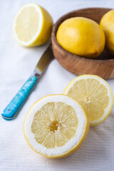 Aerial view of half lemons, blue knife and wooden bowl, on white dishcloth, selective focus, vertical