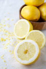Top view of half lemons, lemon zest, and wooden bowl with lemons, on white dishcloth, selective focus, vertical