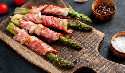 
Baked asparagus with bacon and spices on a cutting board on a stone background