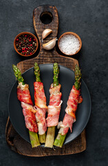 
Baked asparagus with bacon and spices on a black plate on a stone background 