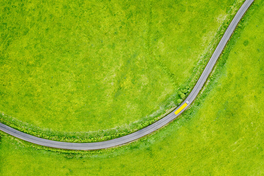 Semi truck with cargo trailer on country road curve among green grass meadow, top down aerial view. Transportation and logistics background with copy space