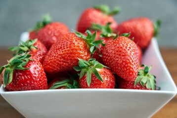 Fresh ripe delicious strawberry in a white bowl on brown wooden table, selective focus.