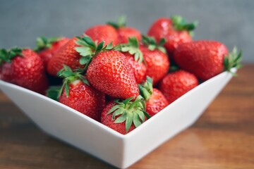 Fresh ripe delicious strawberry in a white bowl on brown wooden table, selective focus.