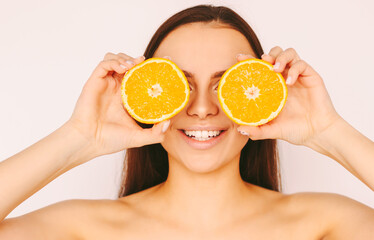 Beautiful young funny girl posing with slices of orange and smile isolated on white background. Happy attractive woman with perfect clean skin have fun with citrus fruit. Beauty procedures, peeling