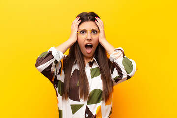 young pretty woman feeling horrified and shocked, raising hands to head and panicking at a mistake...