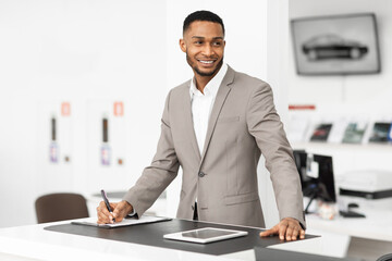 Auto Dealer Standing At Counter Working In Dealership Office
