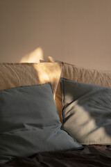 detail of beige and light blue pillows over a cozy bed with sunlight